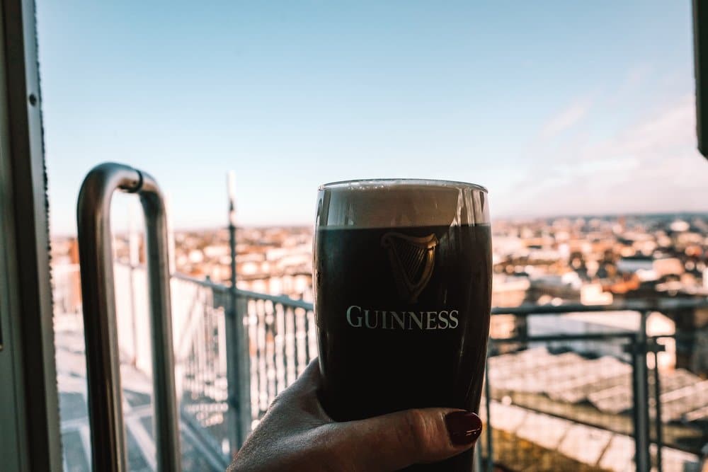 A woman hand holding a guiness beer with irleand city in the background