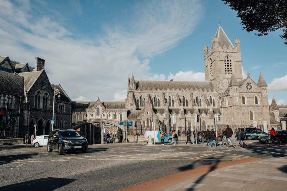 Busy street scene in front of the historic Christ Church Cathedral in Dublin, with pedestrians and cars passing by, highlighting the dynamic blend of daily life and ancient architecture, ideal for solo travelers immersed in the city's heritage.
