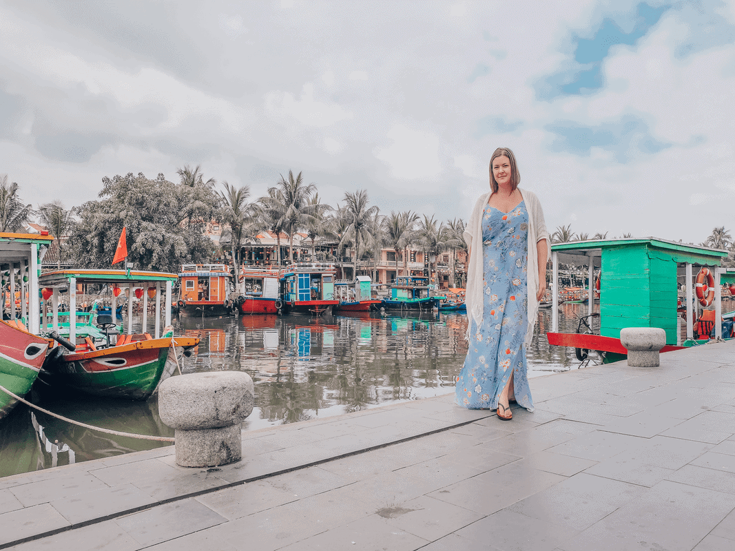 7 Reasons Why Solo Travel Is Better After 35, a woman walks alongside a canal filled with brightly-colored boats.