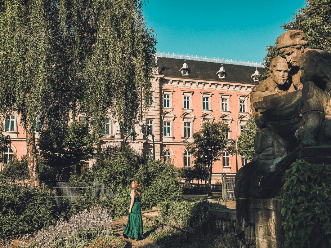 7 Reasons Why Solo Travel Is Better After 35, a woman walks through a lush garden in front of an old brick building.