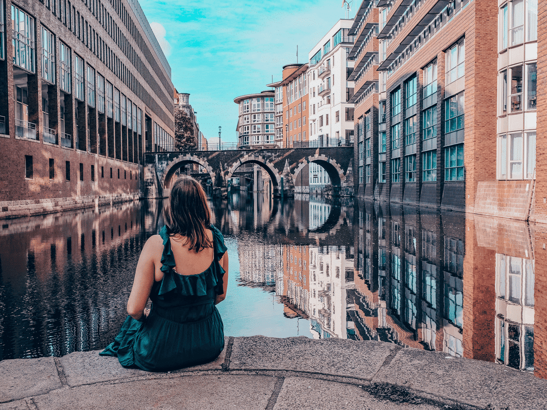 7 Reasons Why Solo Travel Is Better After 35, a woman sits along the canal of an old European city.