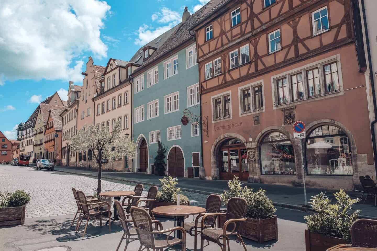An inviting outdoor cafe setting in Rothenburg od der Tauber historic town square, with colorful buildings under a clear blue sky, awaits visitors looking for a quaint spot to relax.