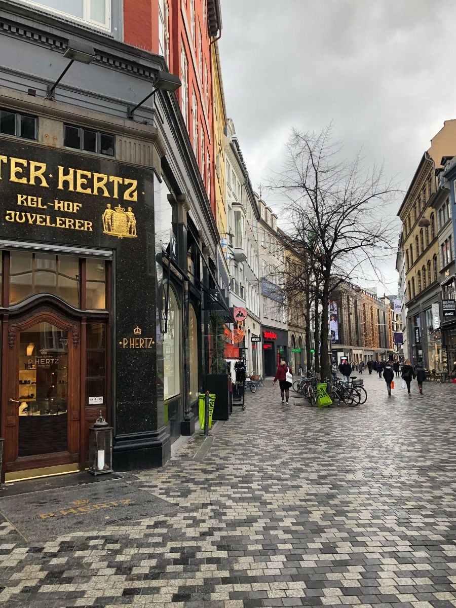 Pedestrian street along Str&oslash;get in Copenhagen with shops, bicycles, and people walking through the city center.