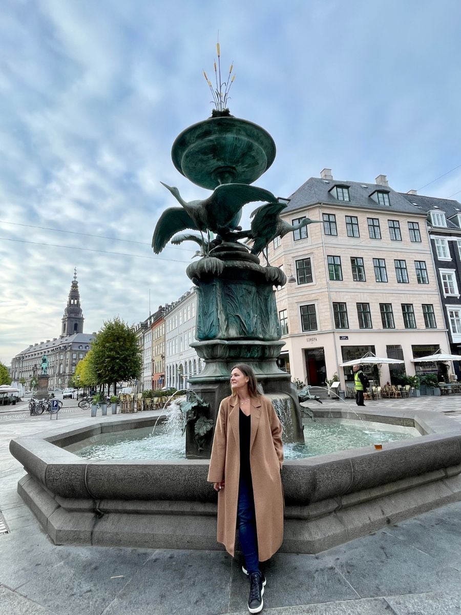 Solo female traveler standing by a historic fountain in Copenhagen&rsquo;s city center.