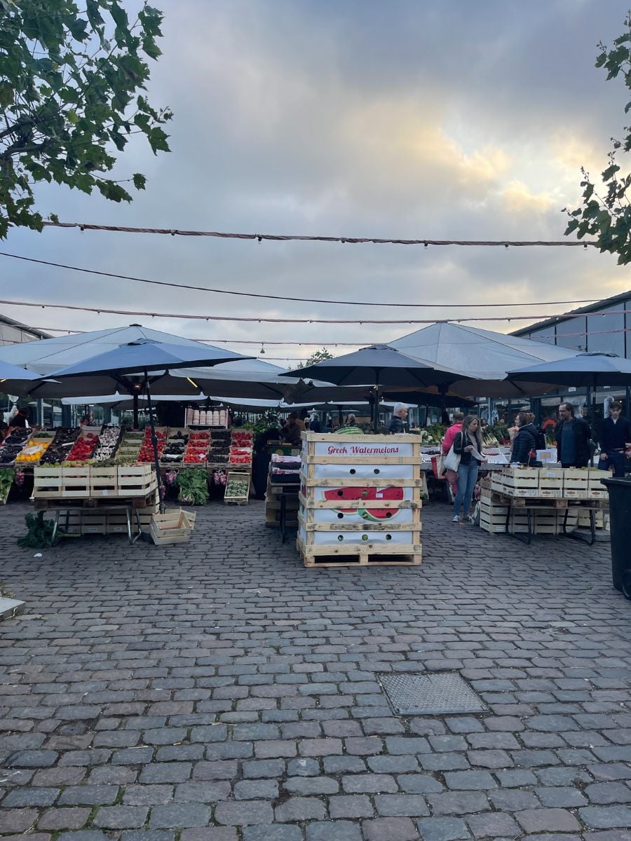 Outdoor produce market in Copenhagen with fruit stands, umbrellas, and locals shopping.