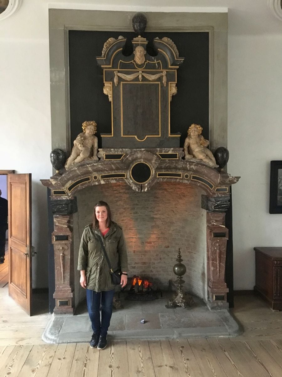 Solo female traveler standing in front of an ornate historic fireplace inside Kronborg Castle in Helsing&oslash;r, Denmark.