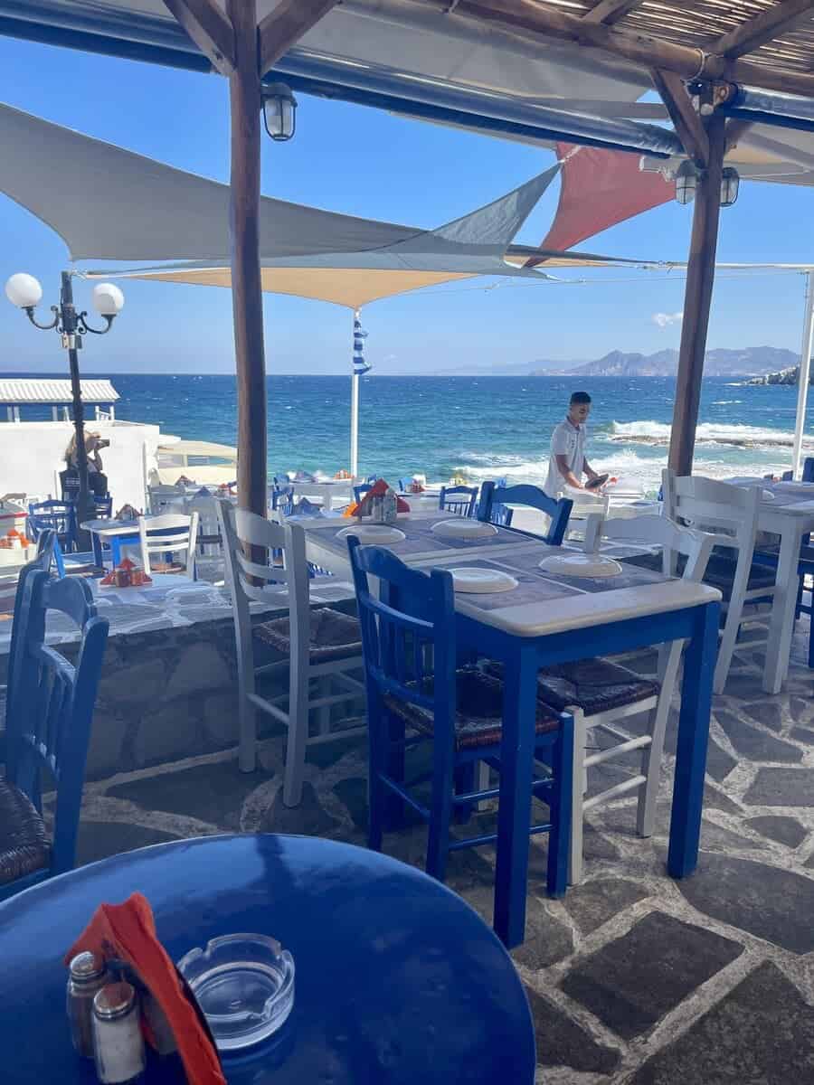 Tables and chairs set for lunch with the background of the ocean. A perfect place for lunch on your Milos itinerary.