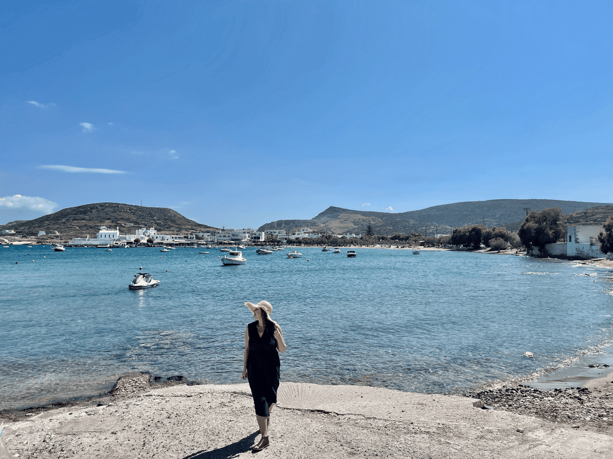 A woman in Milos wearing a hat by the ocean with lots of little boats in the water.