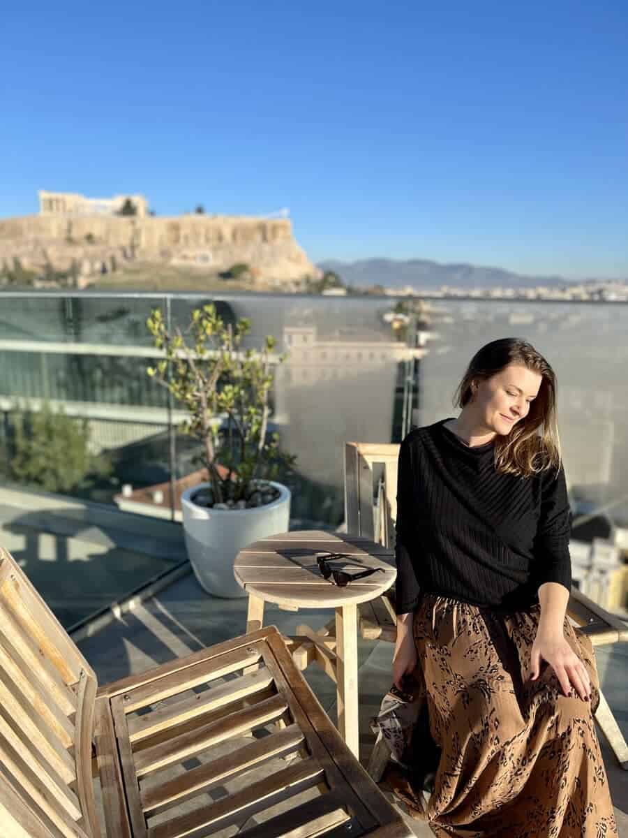 A woman in Athens sitting on the rooftop with the Acropolis in the background