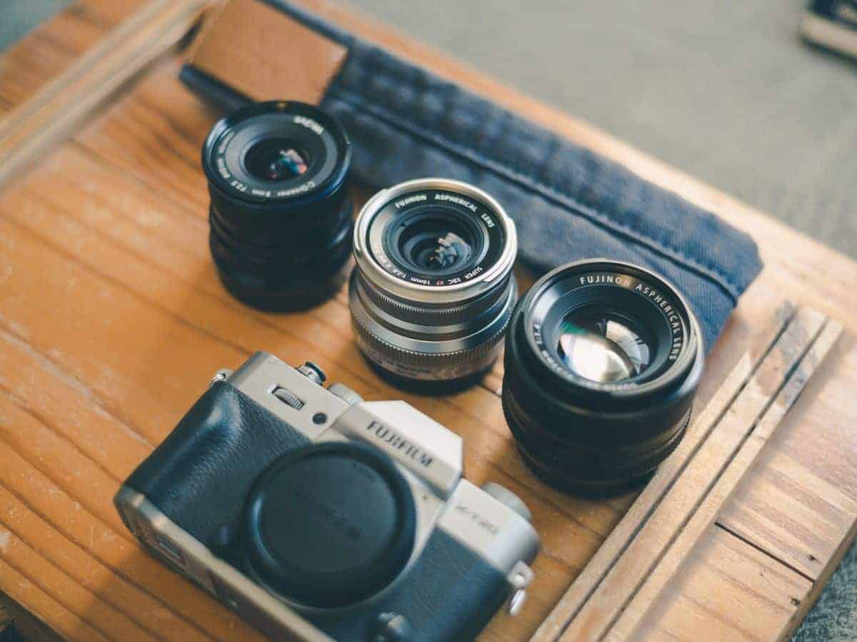 Assortment of Fujifilm camera and lenses on wooden surface, showcasing a lightweight and versatile setup ideal as the best camera for solo travel.