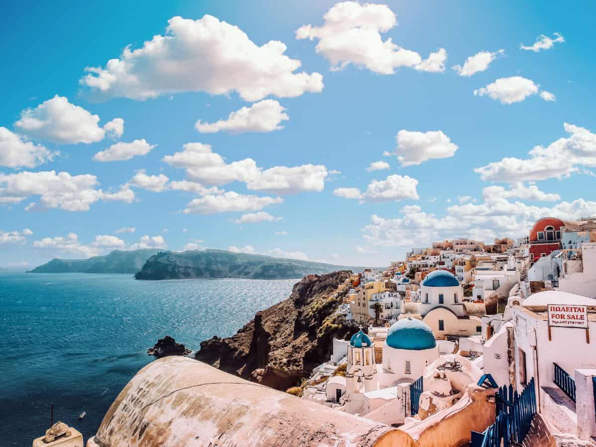 A picturesque view of the cliffside village of Oia on Santorini Island, Greece. The scene showcases traditional Cycladic architecture with white buildings and blue domes overlooking the Aegean Sea.