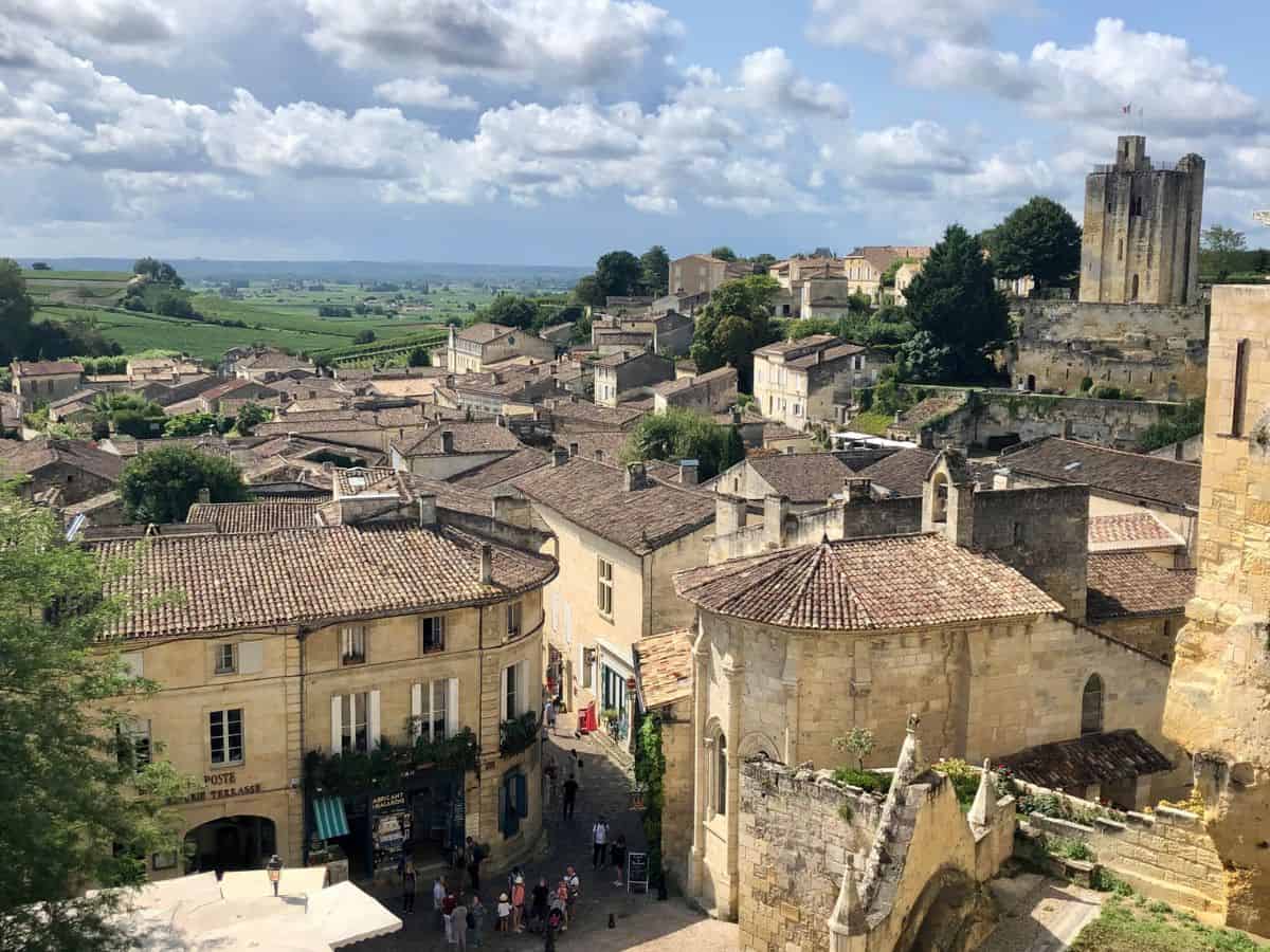 Overlooking the historic village of Saint-Emilion, bustling with tourists exploring the cobbled streets amidst the famous vineyards under a clear blue sky, perfect for the best wine tours.