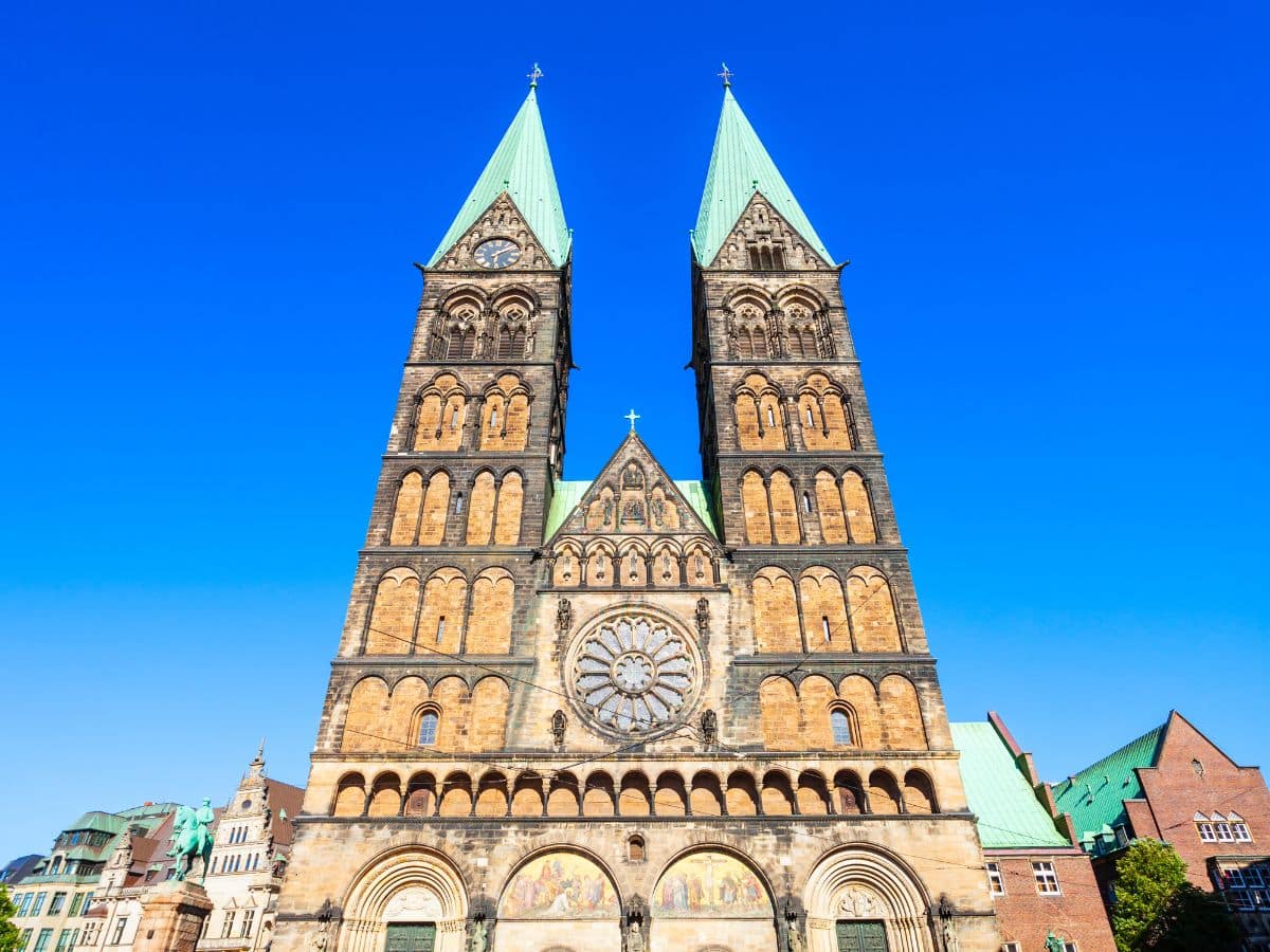 The Bremen Cathedral (Bremer Dom), a striking example of Gothic architecture with its two towering spires, dominates the photo. The cathedral’s façade features a large rose window and multiple arched windows, with detailed stone carvings adorning the entrance.