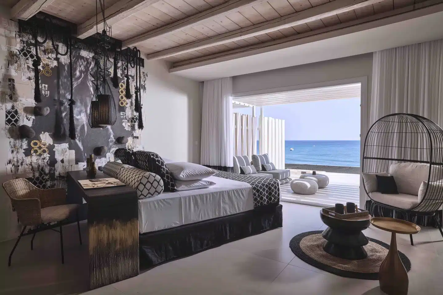 A luxurious room with a chic, modern interior design, featuring a unique wall art installation, elegant furniture, and large windows offering an unobstructed view of the serene blue sea, harmonizing contemporary style with natural beauty.