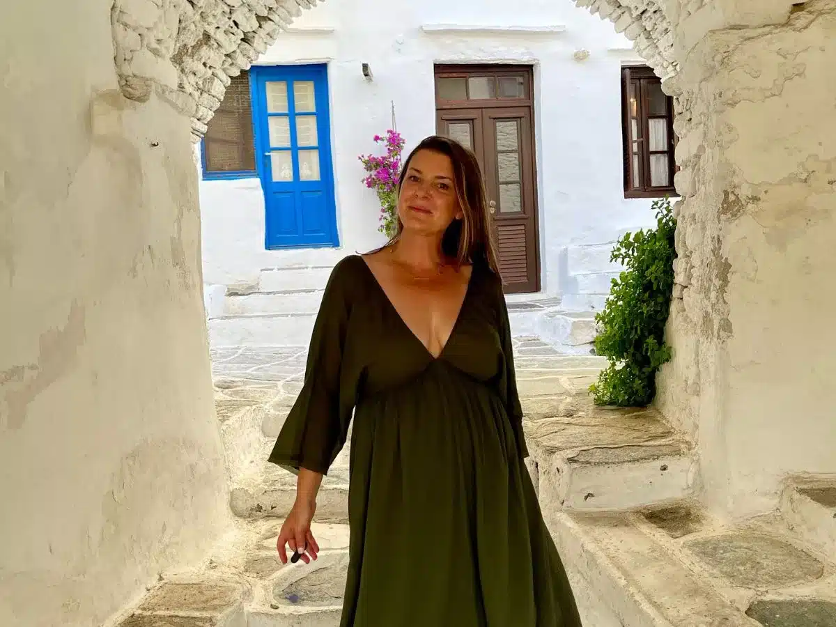 A woman in a green dress stands by a traditional whitewashed stone wall with a blue door, embodying the serene charm of European travel.