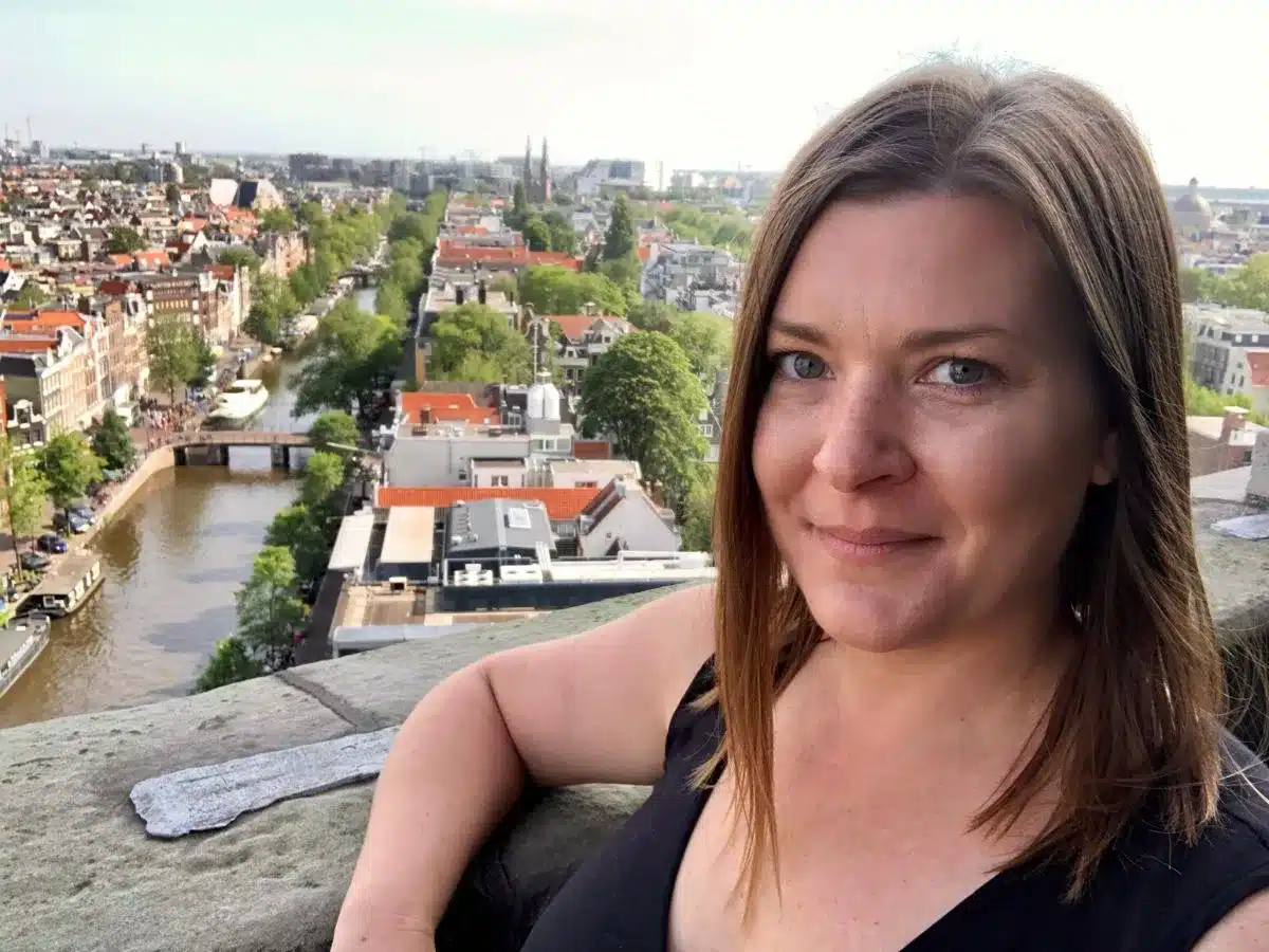 A woman in Amsterdam at the top of a church with the city skyline below her. 