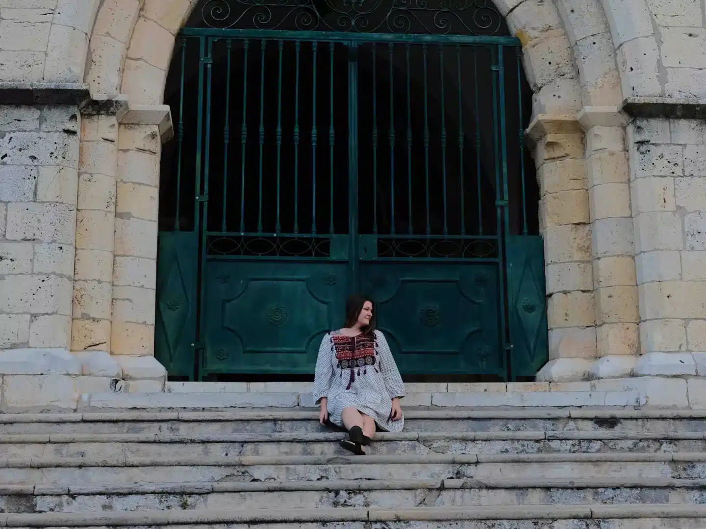 A woman sitting solo on the steps of a church in Faro, Portugal.