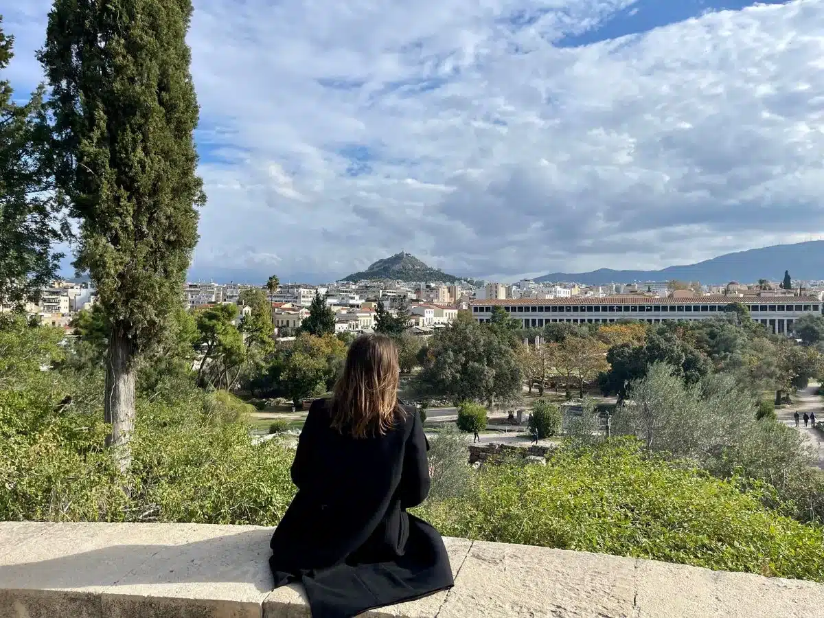 A woman sitting on a bench in Athens alone with the city in front of her