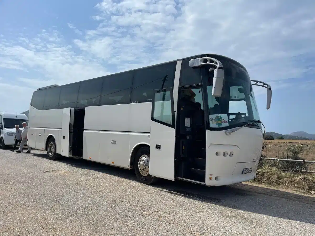 A coach bus parked on the side of a road, ready for a tour on the sunny island of Milos.