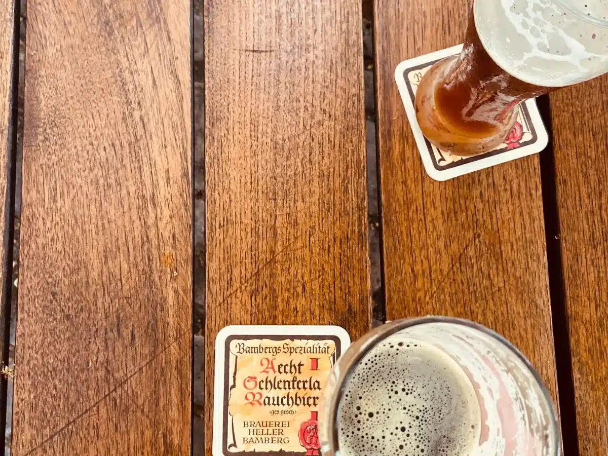 Close-up of a wooden table with two glasses of Bamberg's specialty Rauchbier, a unique smoked beer, inviting travelers to savor local flavors.