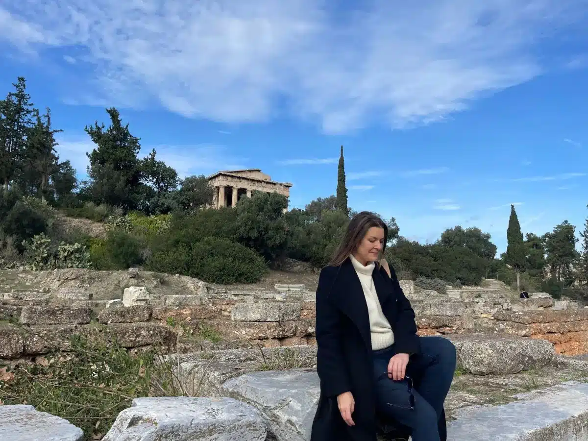 A woman sitting solo in Athens with the ancient buildings in the background