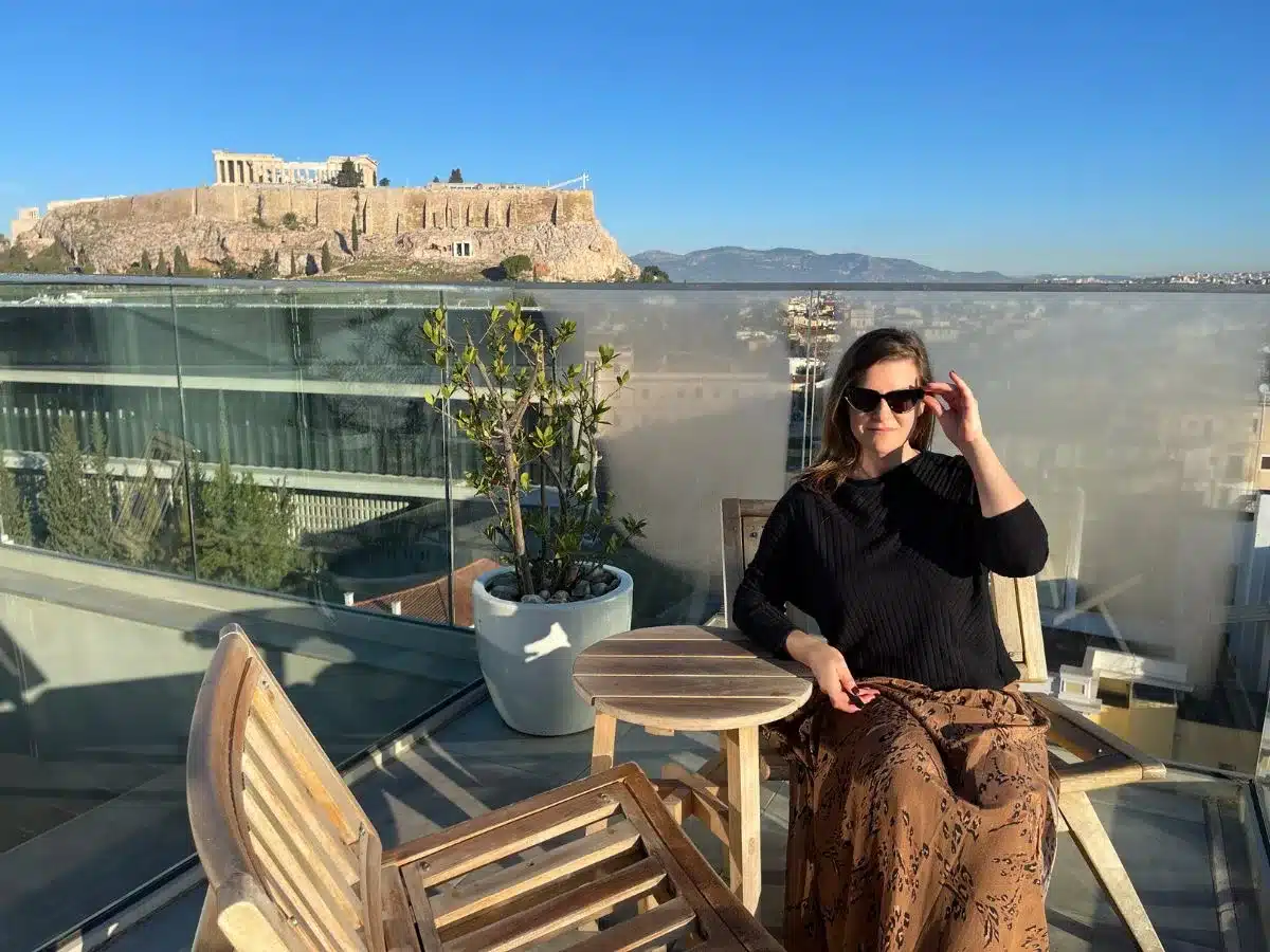 A woman sitting solo in Athens wearing sunglasses with the Acropolis in the background