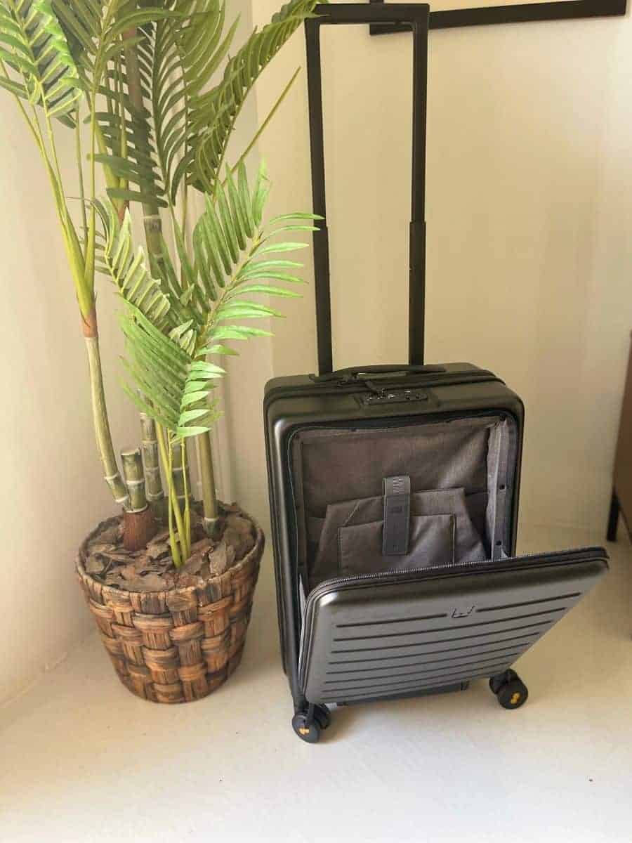 The road runner carry on suitcase open with the space for a laptop. Suitcase is next to a plant