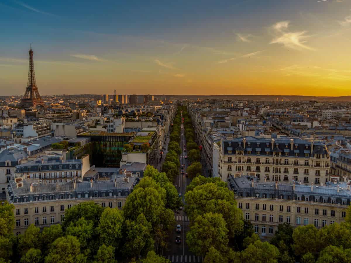 A panoramic view of Paris at sunset with the iconic Eiffel Tower in the distance and a lush, tree-lined avenue stretching toward the horizon, capturing the romantic atmosphere ideal for a solo trip to Paris.