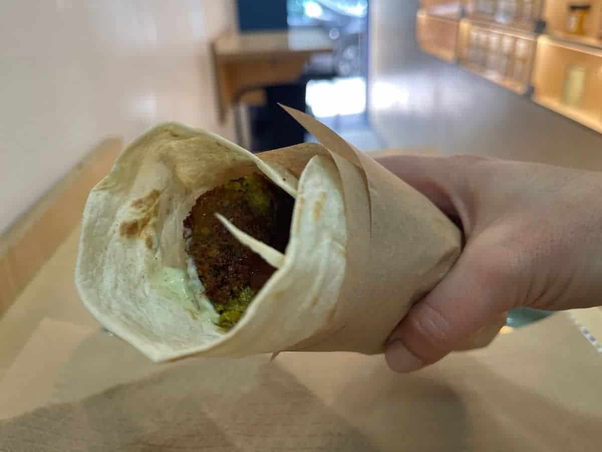 Tips for dining alone is eating street food. A picture of street food falafel in a solo travelers hand