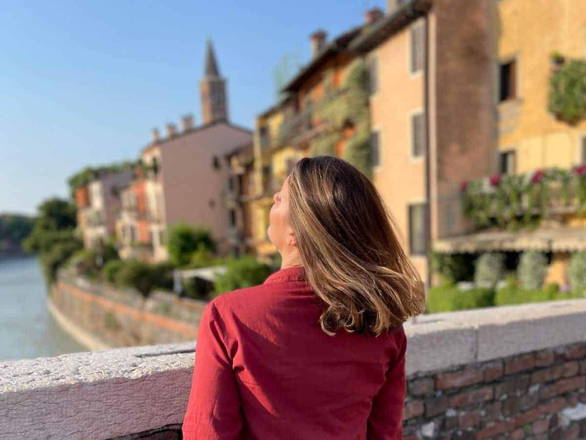 A woman in front of a brick wall with a look at an Italian village in the background
