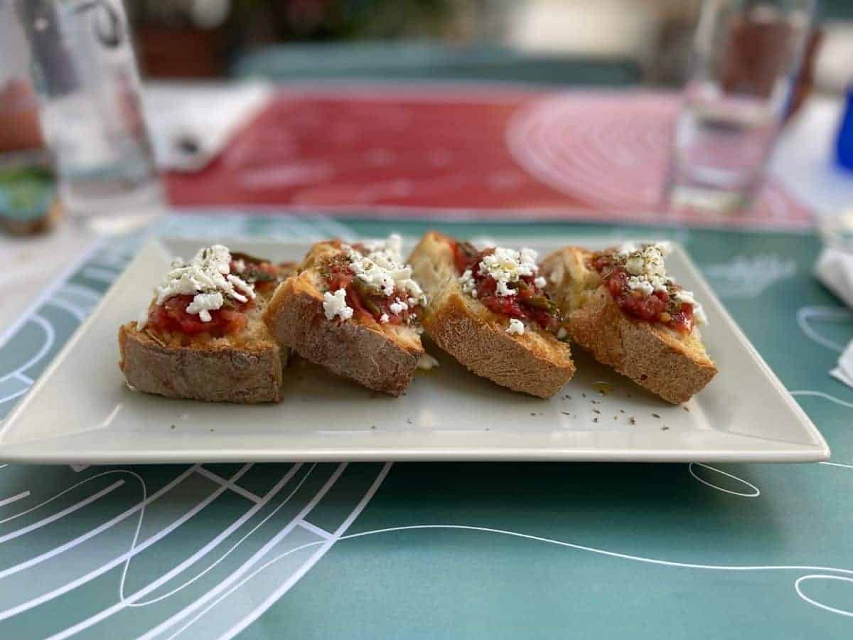Best meals for dining solo is tapas. A white plate with 4 pieces of bread tapas.