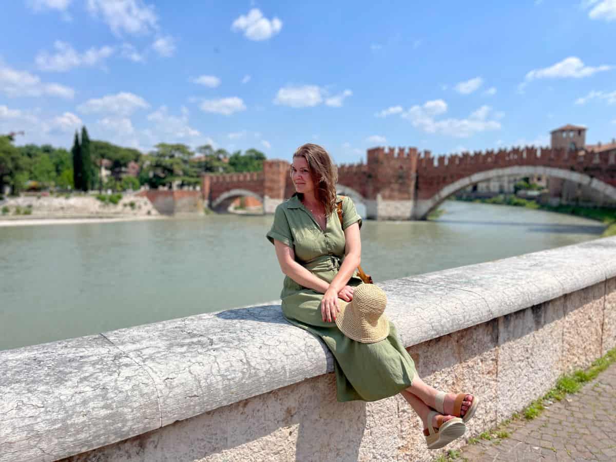 A woman sitting on the ledge of a wall with the river and bridge of verona in the background