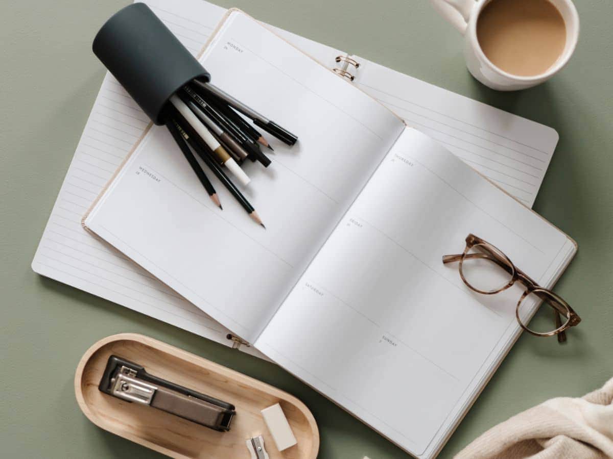 a note book and pens with reading glasses. An office set up to create a travel budget