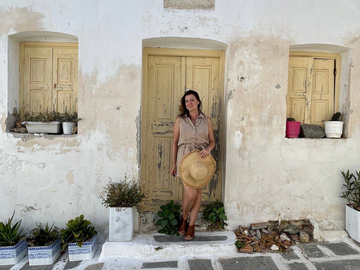 a woman solo in Serifos standing in front a a door holding a hat