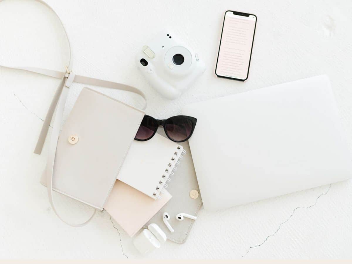 A womans pair of sunglasses and chic purse with office items such as phone, laptop and camera