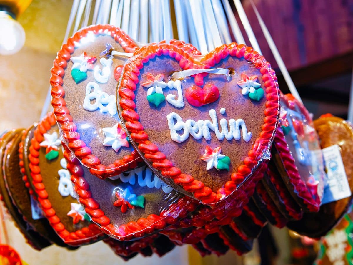 Close-up of traditional heart-shaped gingerbread cookies, decorated with white icing spelling 'I love Berlin,' framed by vibrant red icing and colorful sugar decorations, hanging as festive souvenirs at a Berlin Christmas market stall.