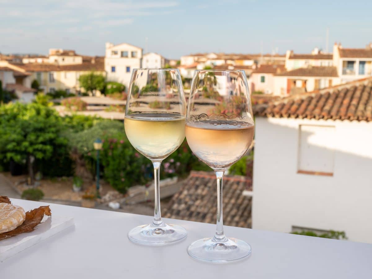 2 glasses of wine sitting on a ledge with the town of Port Grimaud in the background