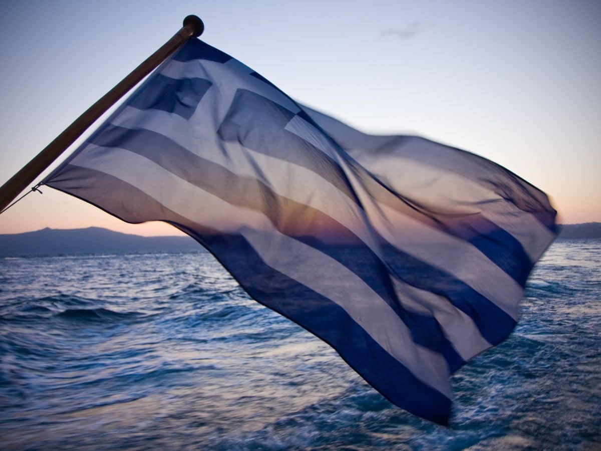Greek flag over the ocean at sunset