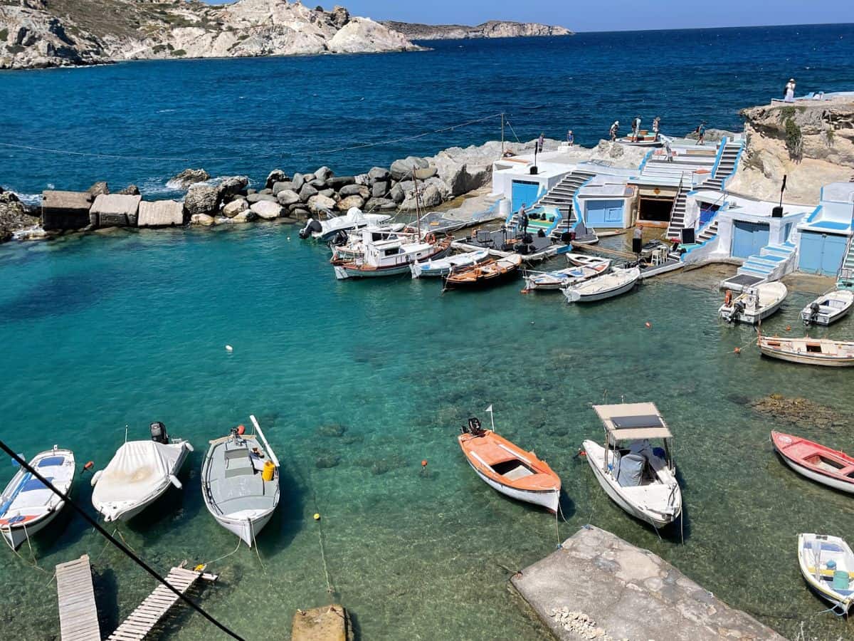 Greek Island of Milos and the crystal blue waters with small boats in the water.