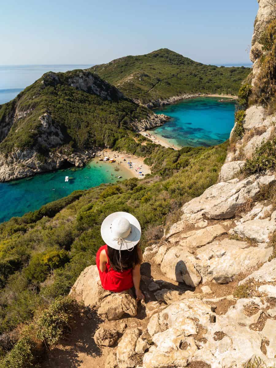 Solo Woman traveling sitting on a rock up overlooking Dubble Bay in Corfu that you need to rent a car to visit