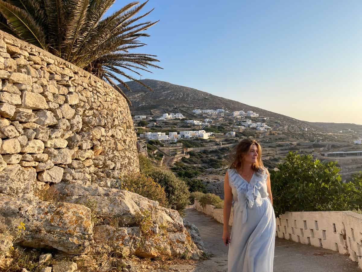 A woman walking alone with the background of mountains and small Greek houses. 