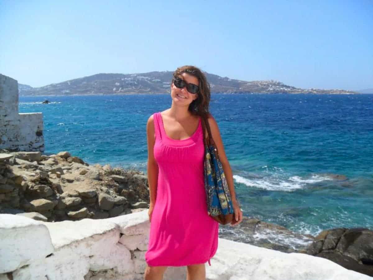 A solo woman traveling in a pink dress in Mykonos in front of the aegean sea!