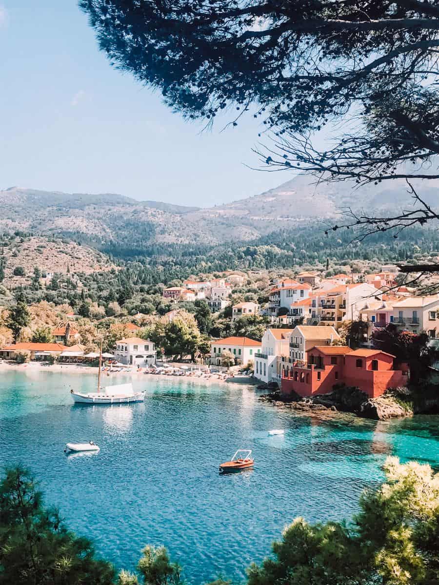 A picturesque cove on the island of Corfu, framed by verdant hills and featuring waterfront homes with terracotta roofs, clear turquoise waters, and boats gently floating, encapsulating the idyllic Greek island charm.