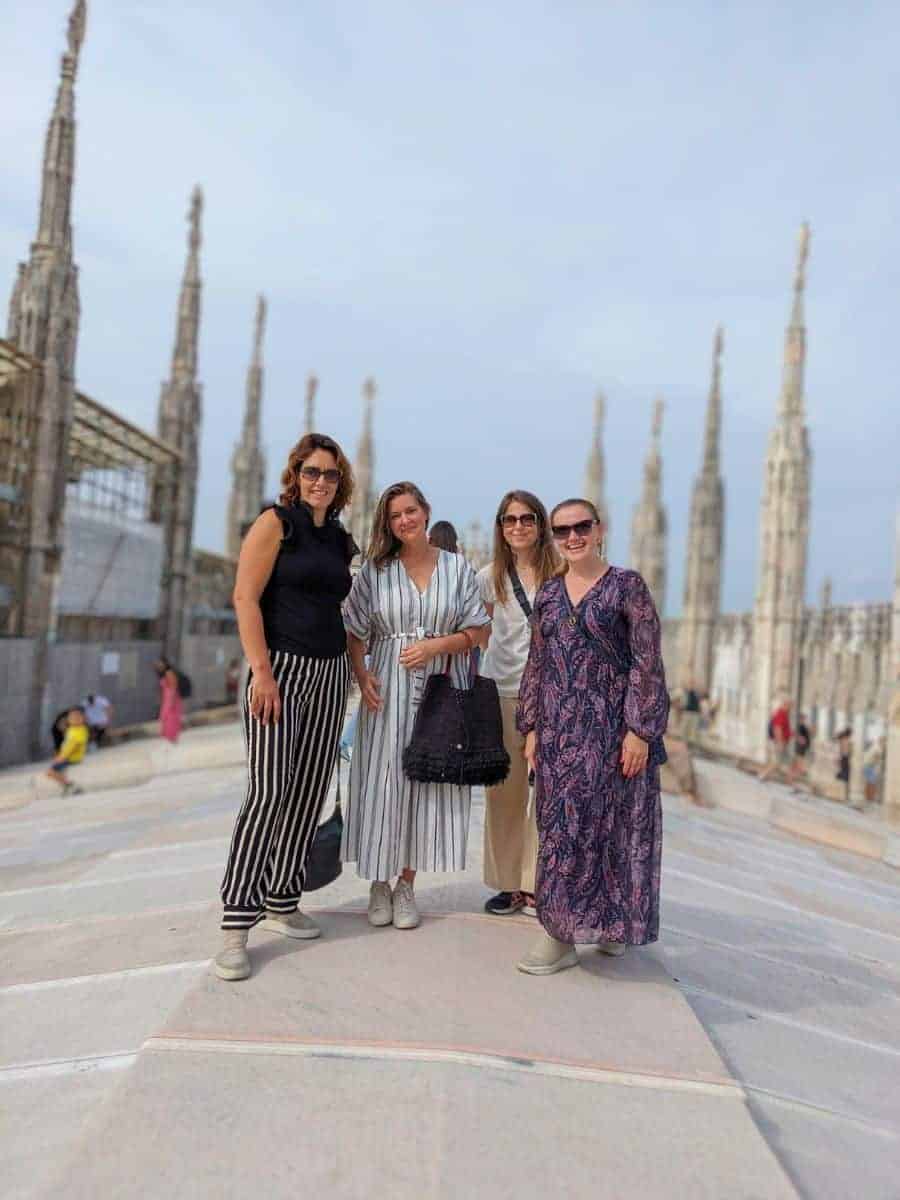 Group of friends in their 40s enjoying the company and architecture on the rooftop of Milan's cathedral, showcasing the joy of shared travel experiences.