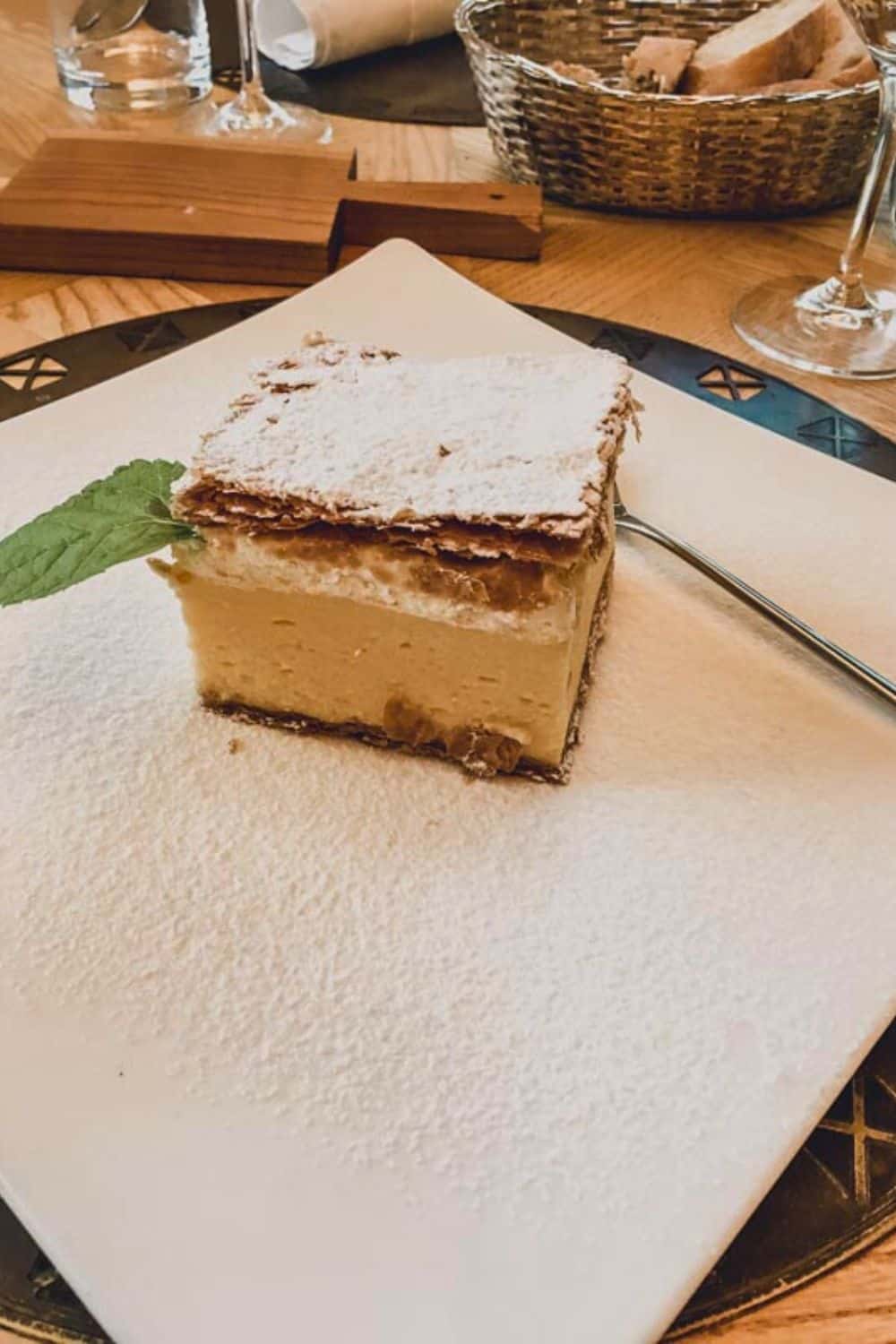 A classic piece of Bled cream cake, known as 'kremšnita,' dusted with powdered sugar and served on a white plate, symbolizing Slovenia's beloved dessert tradition.
