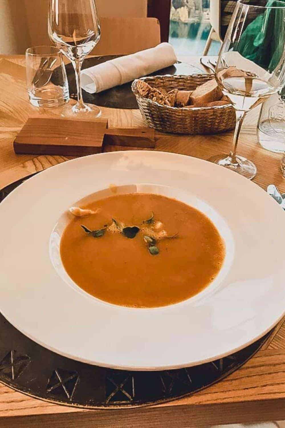 A bowl of rich, creamy soup served elegantly in a white bowl, paired with a basket of bread and a glass of white wine, ready for a gourmet experience