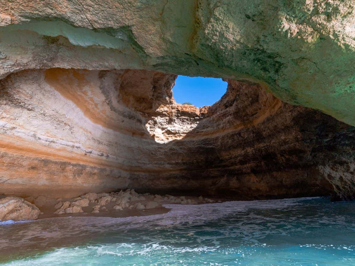 Inside view of a majestic sea cave along the Algarve coast near Faro, with sunlight filtering through the opening, illuminating the textured rock layers and turquoise waters below, a stunning natural wonder to explore on a day trip from Faro.