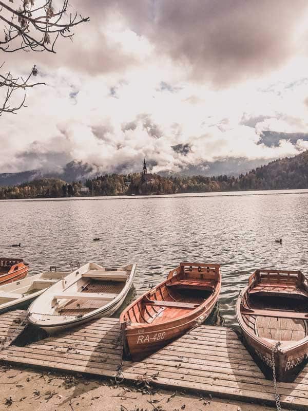 Wooden boats docked at the frosty shores of Lake Bled, with the misty silhouette of Bled Island in the distance, ready for a winter rowing adventure.