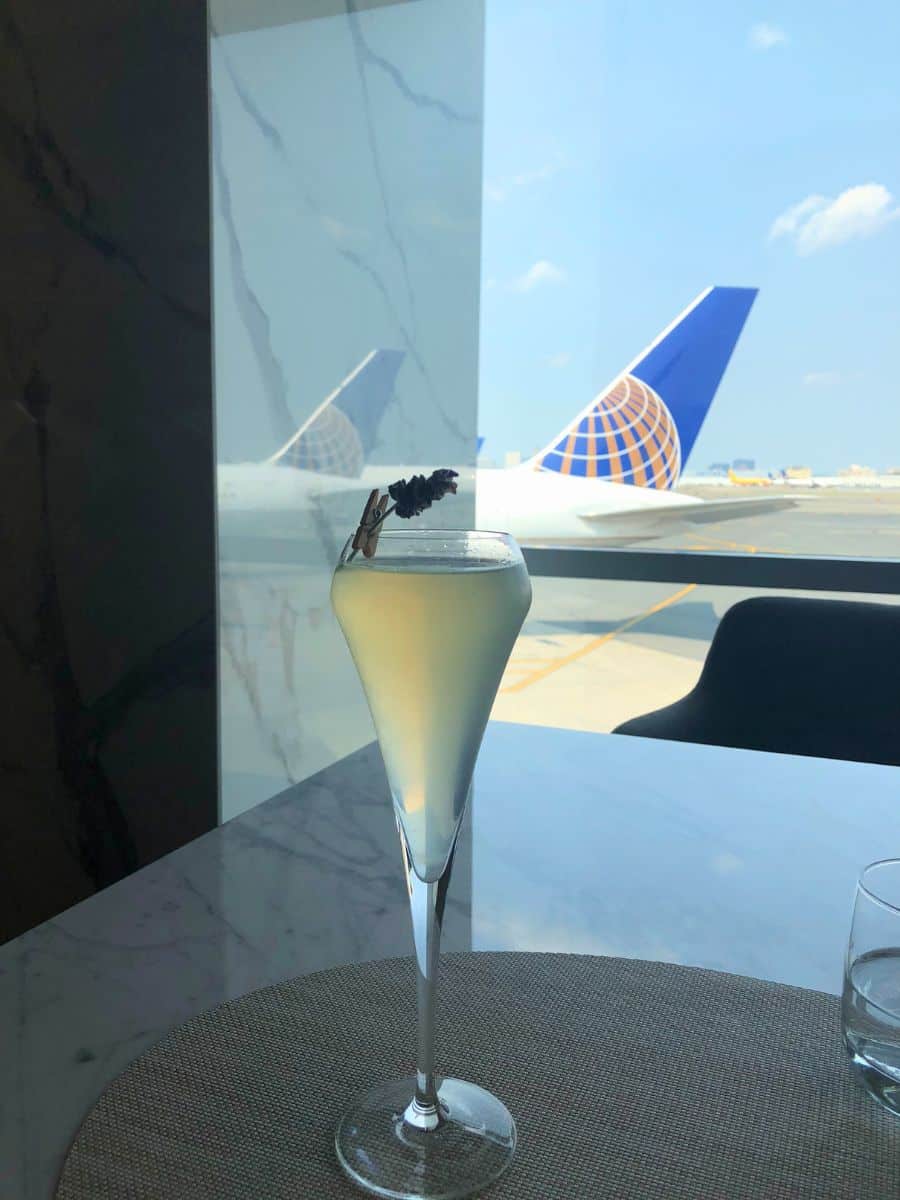 Close-up of a chilled glass of champagne with a lavender sprig on a marble table, overlooking the iconic tails of airplanes through the window of an airport lounge, capturing the essence of luxury travel that Priority Pass membership might offer