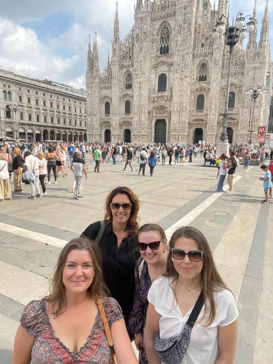 Four happy women friends posing together with Milan Cathedral in the background, enjoying the vibrant atmosphere of Piazza del Duomo.